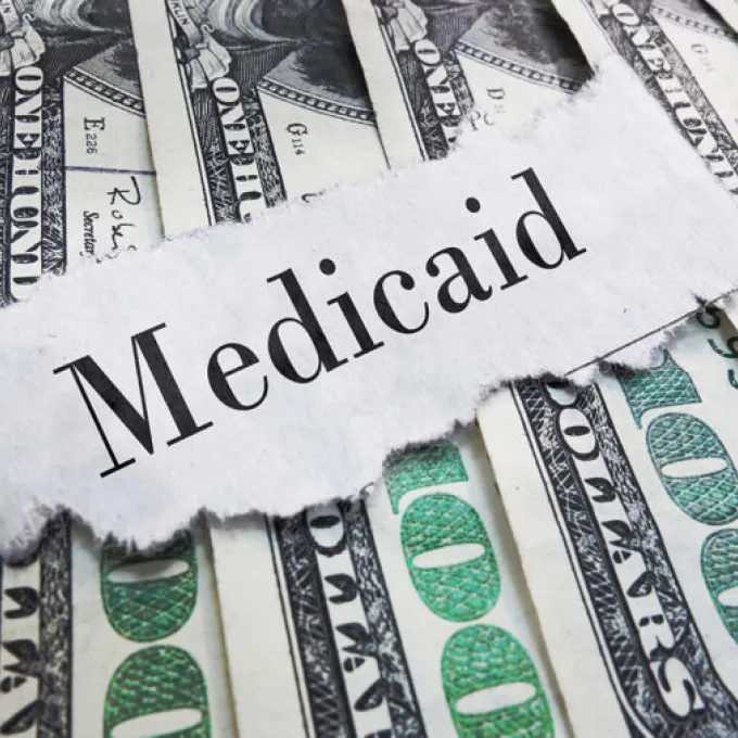 a ripped piece of newsprint ominously reading "Medicaid" placed over a pile of money