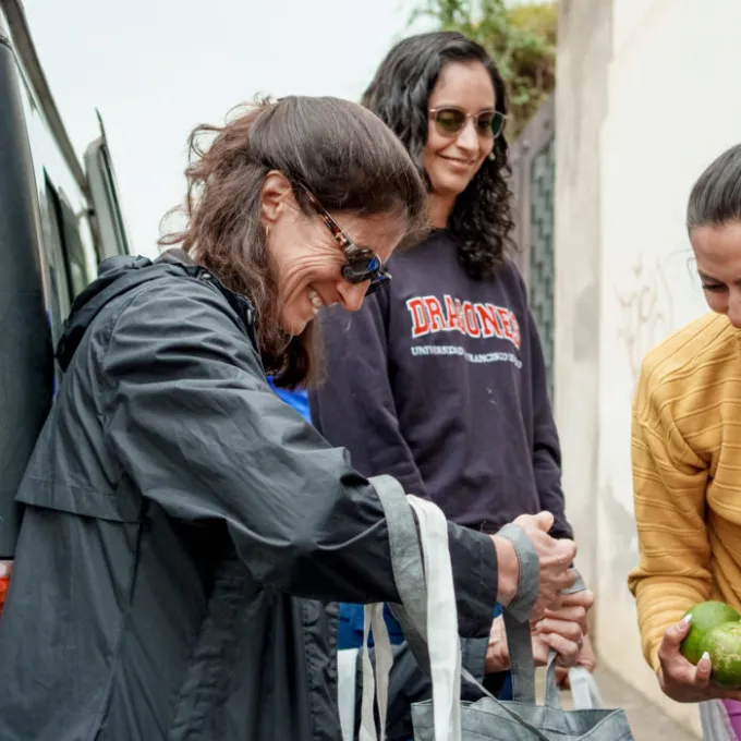 Lora Iannotti (left), Gabriela Vintimilla, MD, and Karen Ballardes, owner of Amazonic Gardens organic farm, fill bags with fresh vegetables, fruit, eggs and fish for expectant mothers at El Quinche Clinic. (Photo: Whitney Curtis/WashU)